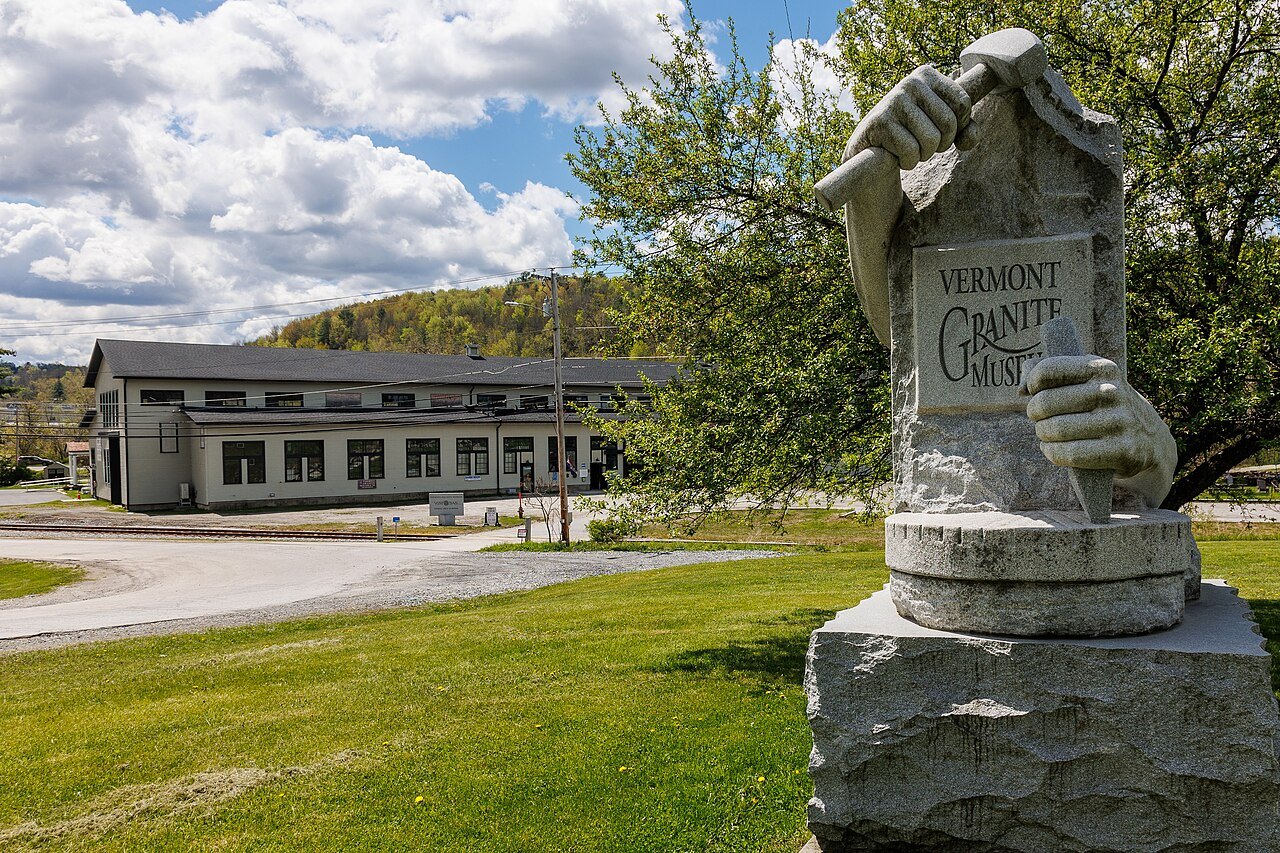 A granite sculpture of a gloved hand holding a tablet, in front of the Vermont Granite Museum.