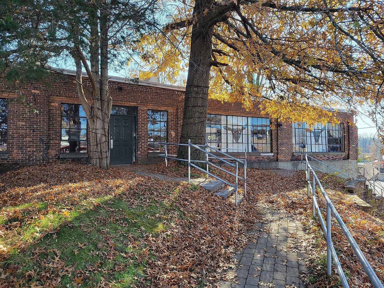 A brick building on a bluff in Bellows Falls, with autumn leaves on the ground and a rail down the steps.