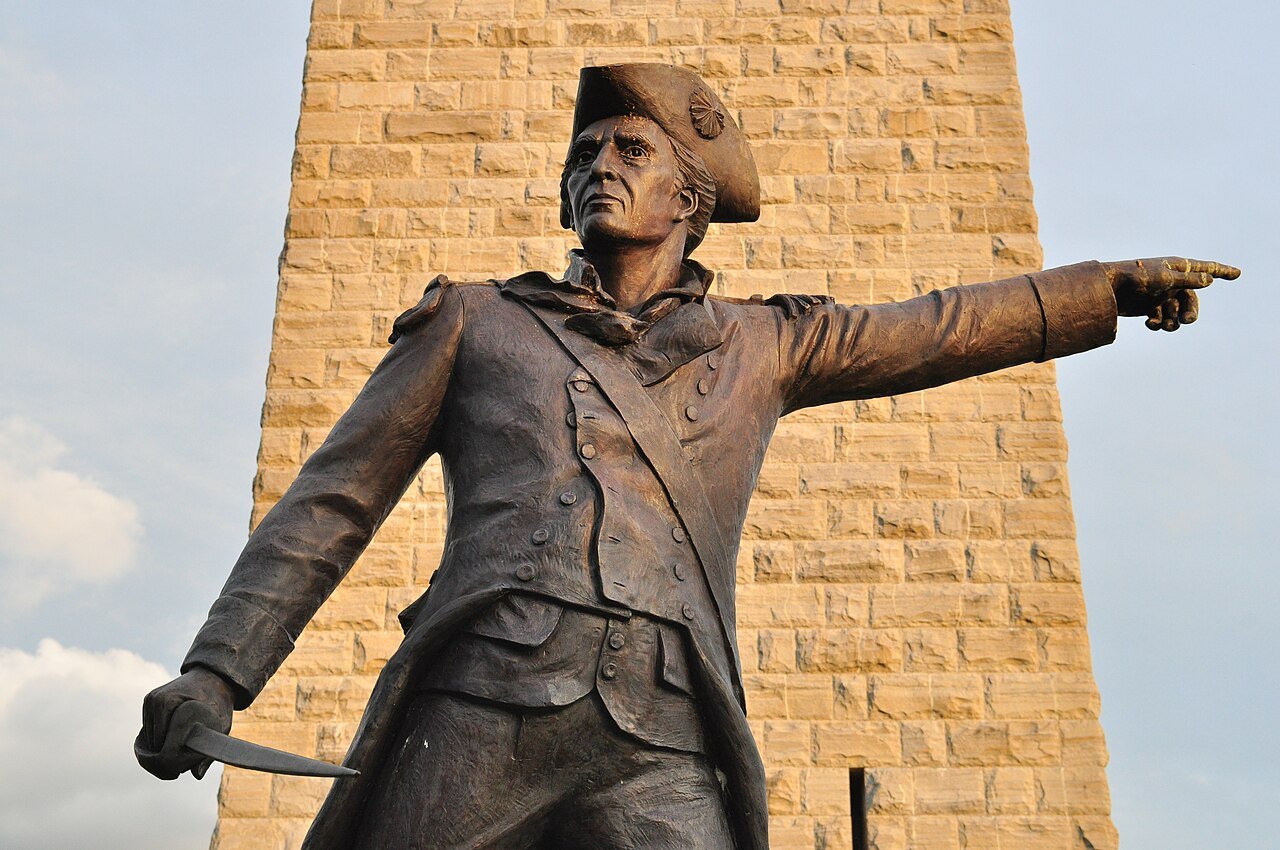 The bronze statue of John Stark, pointing, in front of the monument's stone.