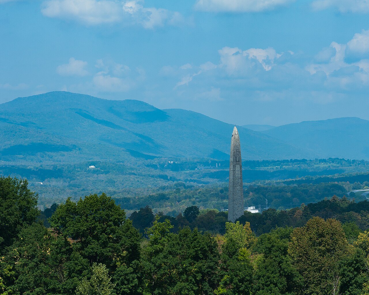 A distant view of the monument over forest, with blue hills behind.