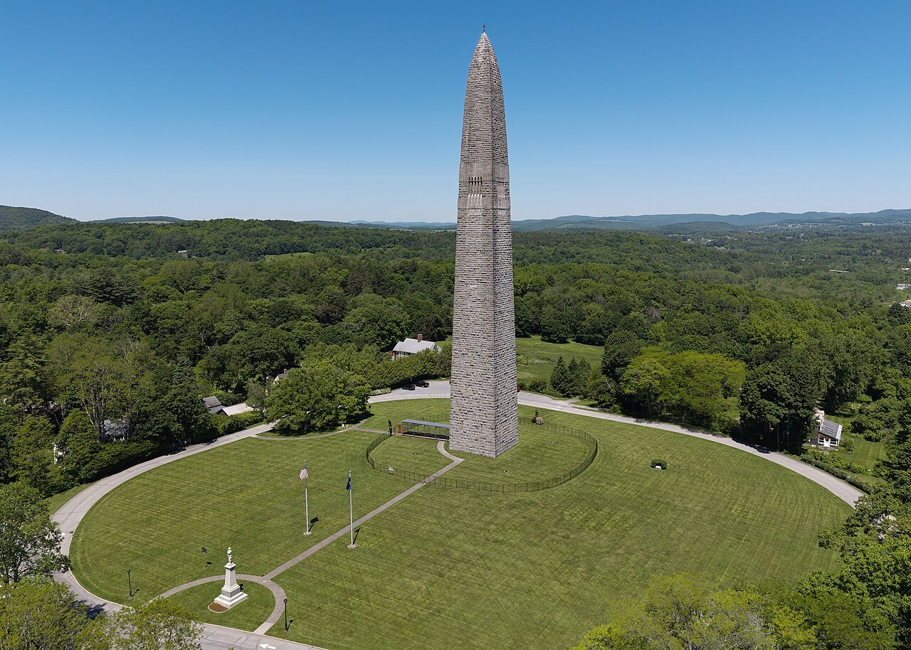 The monument and its circular lawn from above, among green forest.