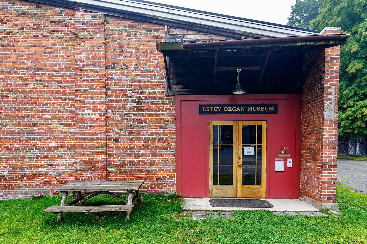 The Estey Organ Museum, a red door in a brick wall with a picnic table in front.