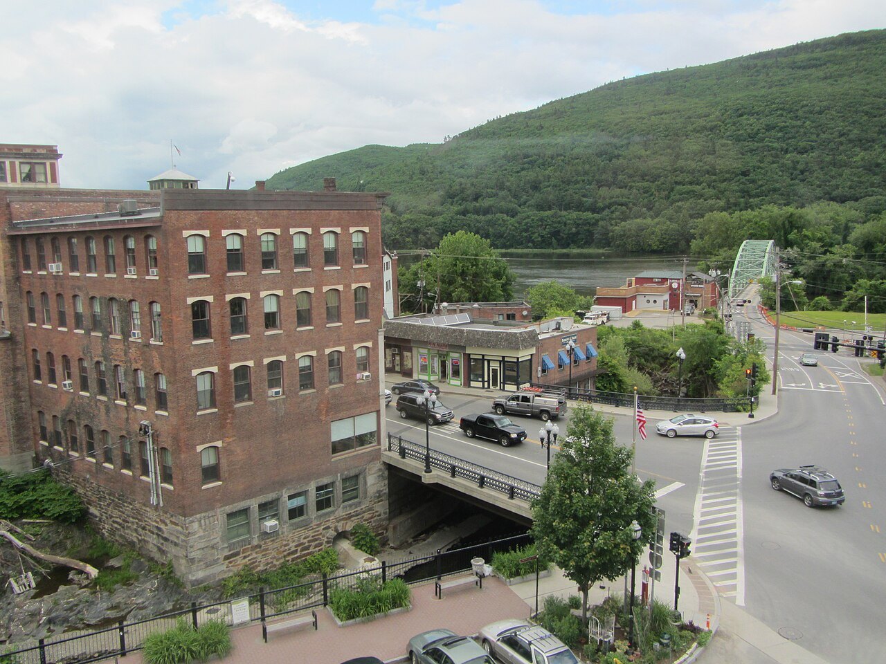 Main Street in Brattleboro from the Coop, a long brick mill building beside a bridge and a hill.