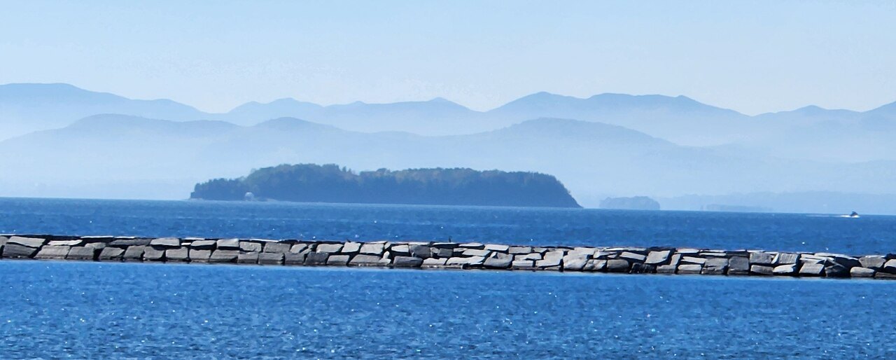 Juniper Island, a low wooded island seen across blue water behind a stone breakwater.