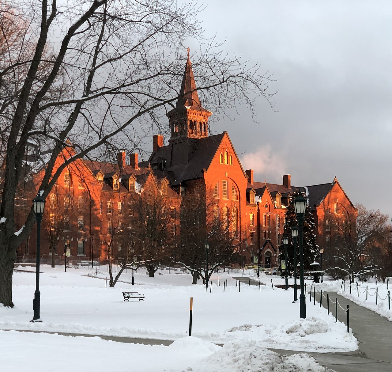 Old Mill at the University of Vermont in winter, its brick glowing orange above a snowy path.