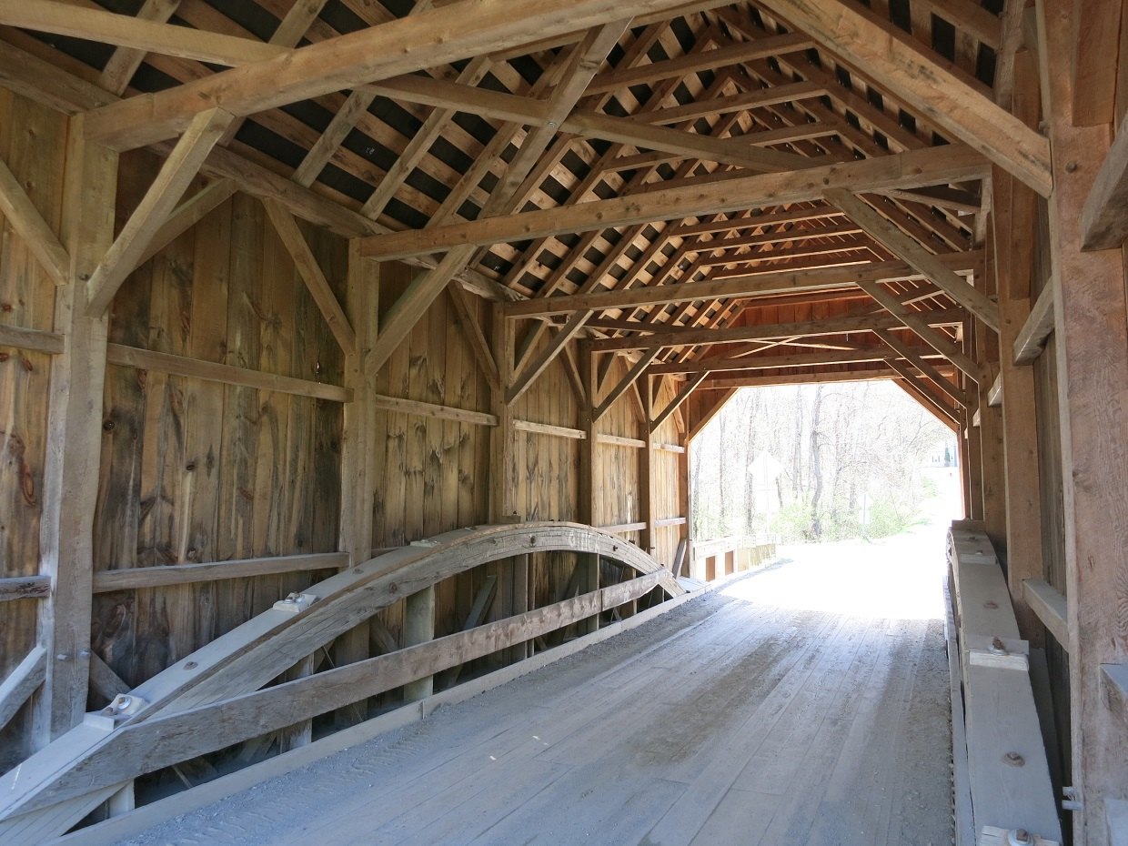 Inside the Bowers Bridge, timber trusses and a white rail curving to the bright far portal.