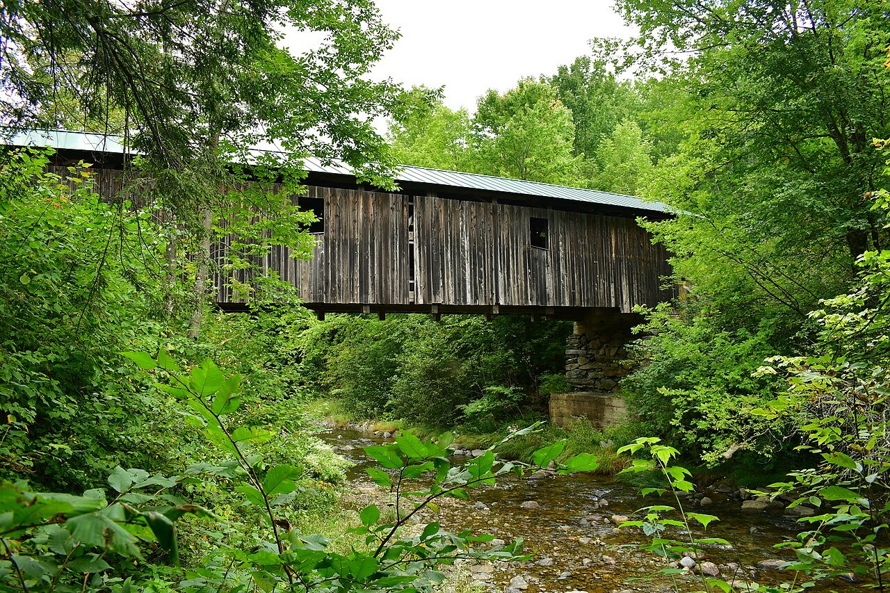 The Grist Mill Bridge in Cambridge, a long gray bridge half hidden by spring leaves.