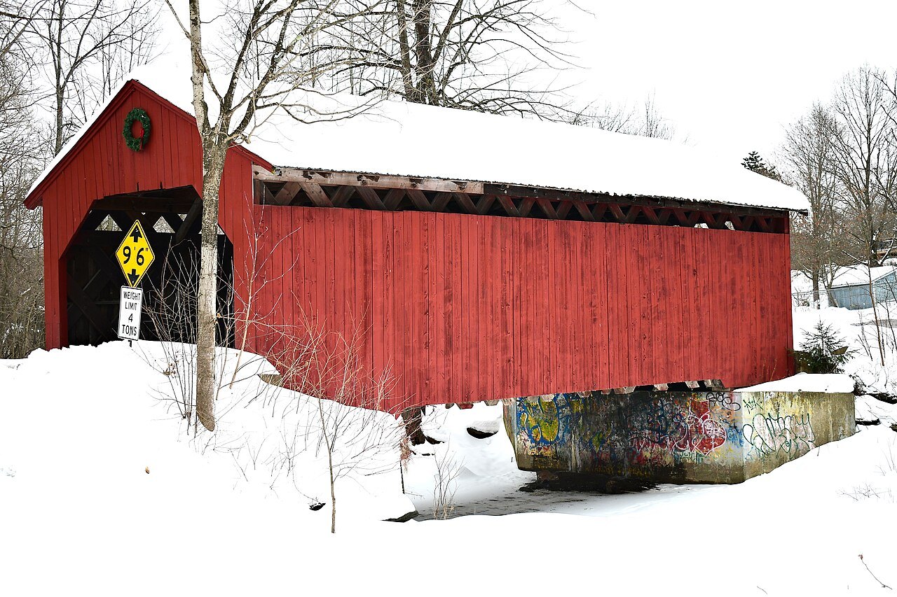 The Maple Street Bridge, red, with snow on its roof and white ground around it.