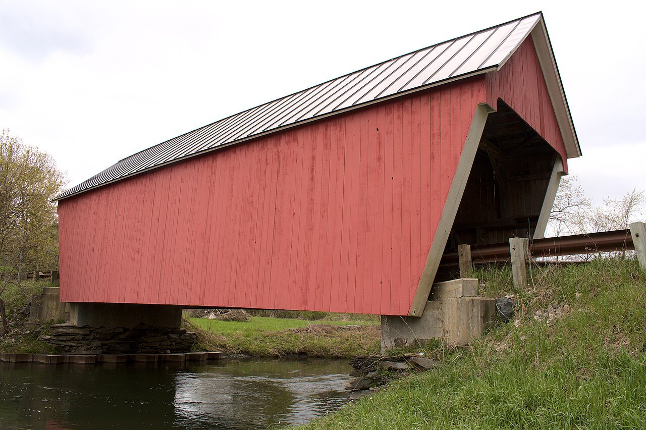 The Gifford Covered Bridge, a red bridge with a metal roof, beside a green bank.