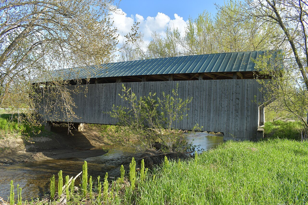 The Gates Farm Covered Bridge, a low bridge with a green roof, over a stream in spring.