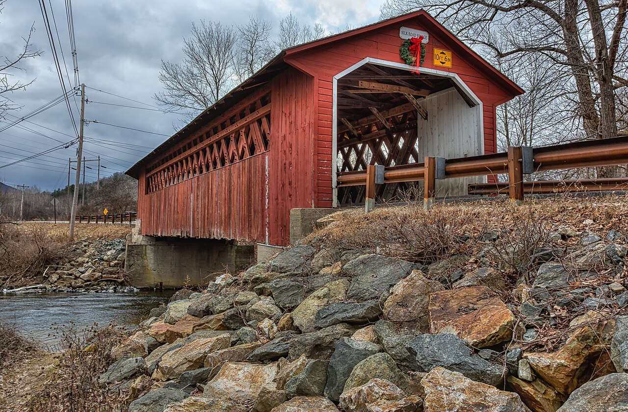 The Silk Road Bridge, a red bridge with a lattice window, beside a rocky bank.
