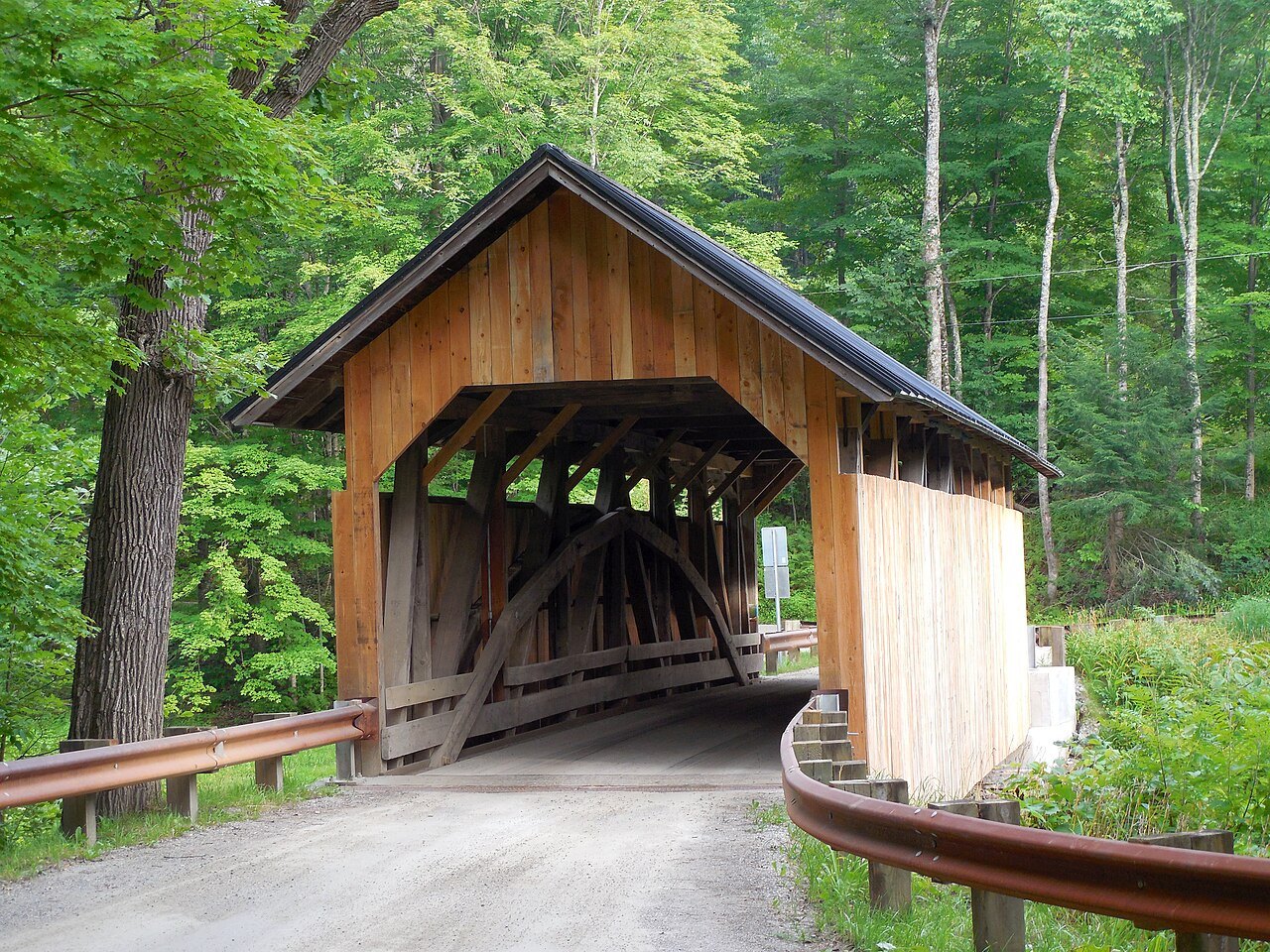 The Sequin Covered Bridge in Charlotte, a timbered bridge with a lattice portal, in green woods.