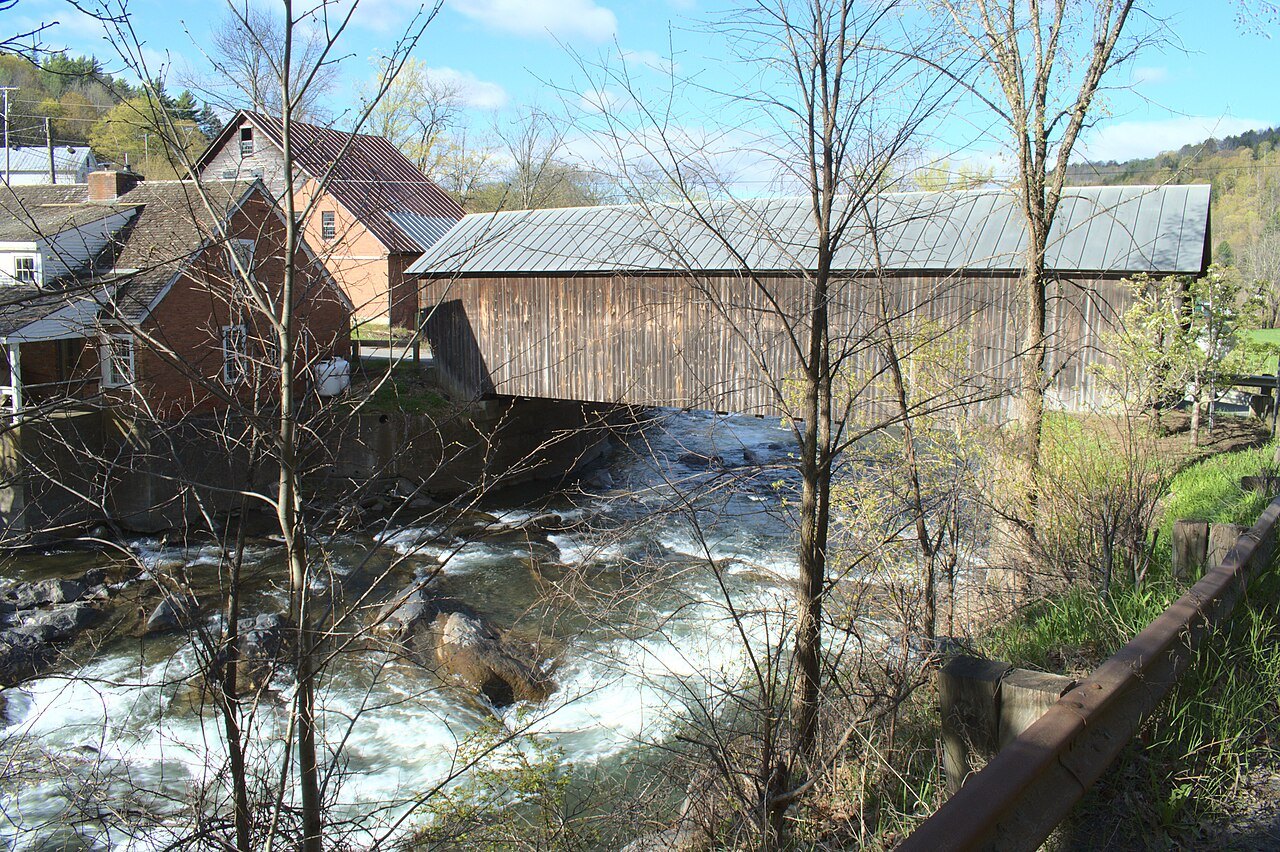 The Mill Covered Bridge above a fall of white water, with a mill building at the left.