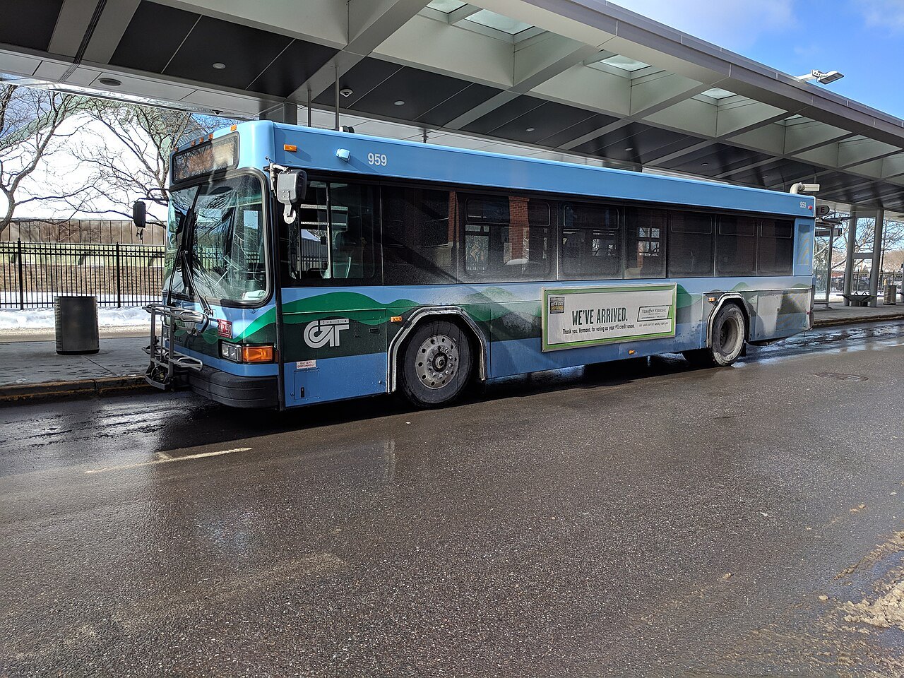 Green Mountain Transit buses waiting under a station canopy in the rain.
