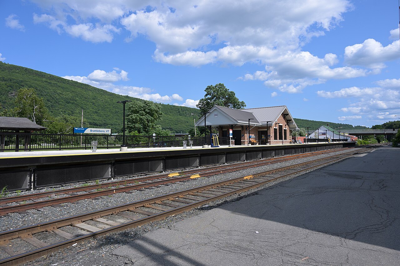 The Brattleboro station platform, a stone depot beside the tracks under a blue sky.