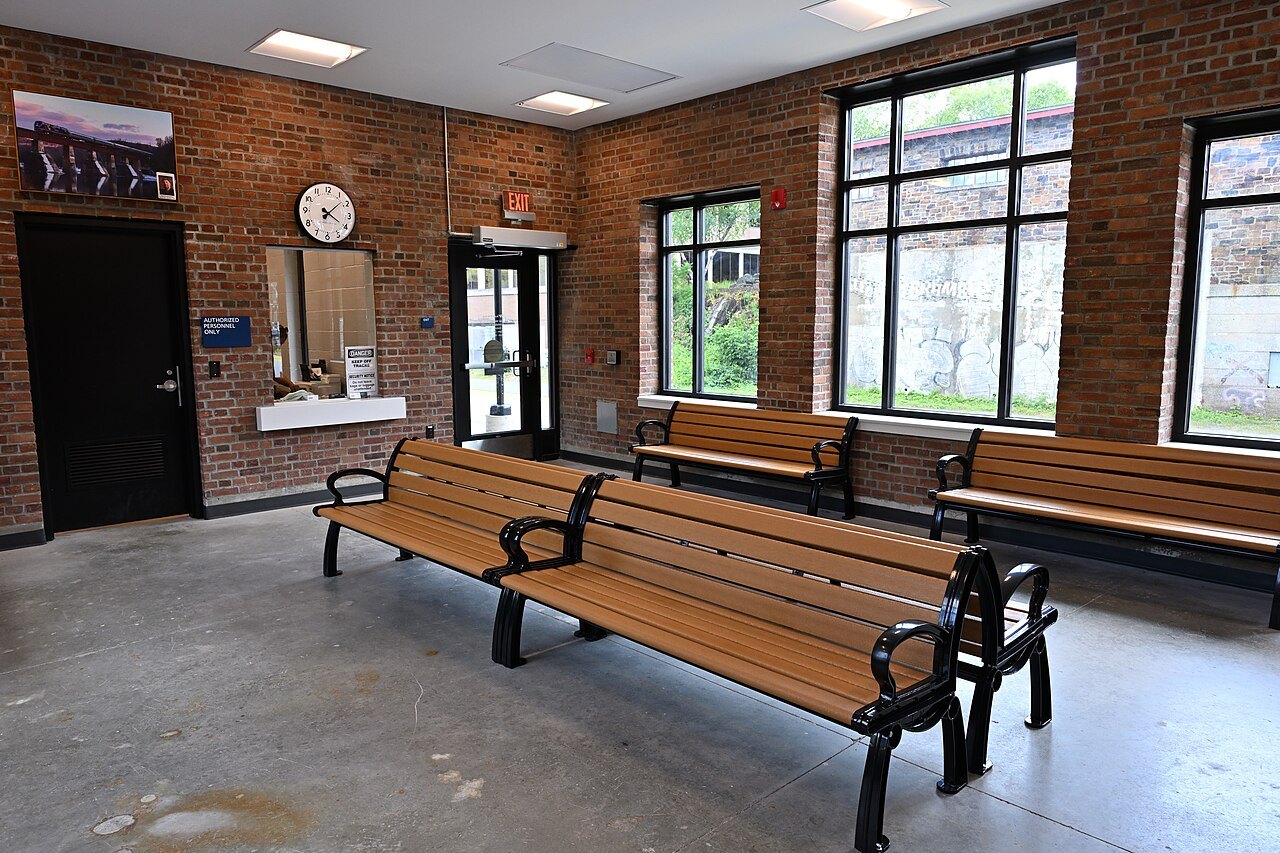 Inside the Brattleboro station, wooden benches under tall windows and a brick wall.