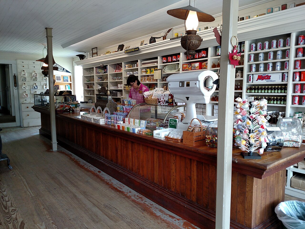 A general store's long counter and shelves, with a clerk at work, kept as it was.
