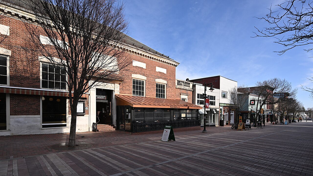 A pedestrian street in Burlington with a brick row of shops and cafés and empty tables.