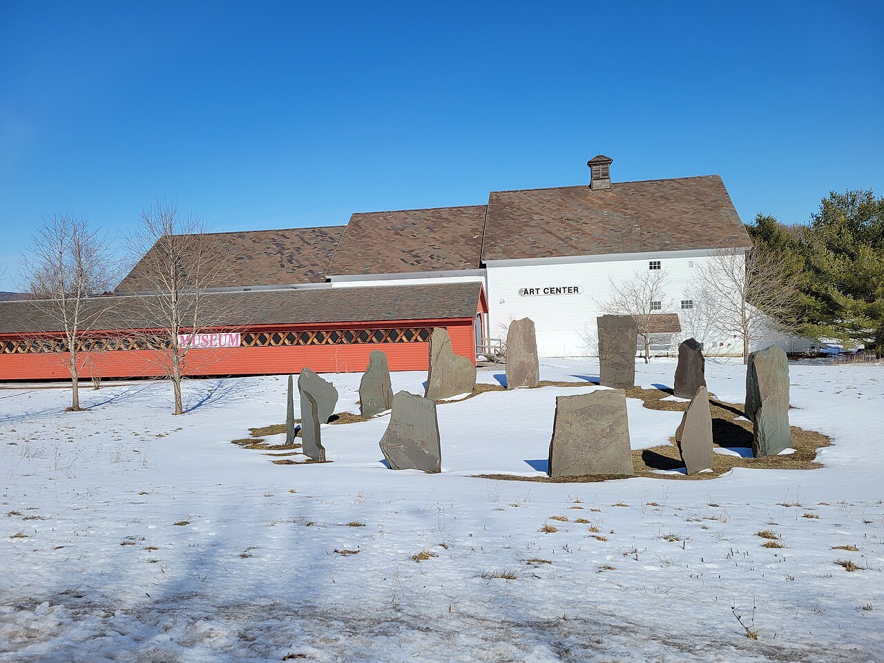 A sculpture park with granite blocks in snow before a white barn.