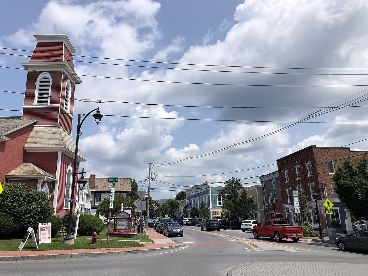 Vermont Route 100 running north through a town with a red church and brick storefronts.