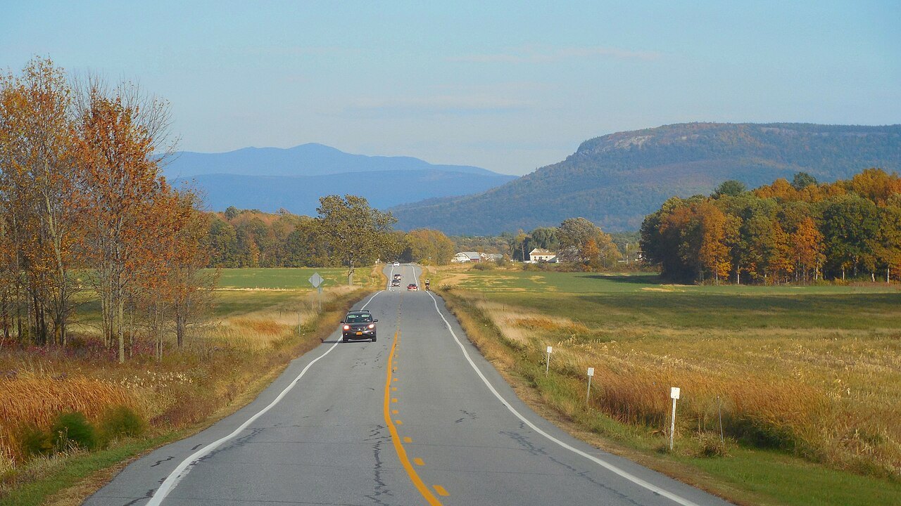 A two-lane road across autumn fields toward Snake Mountain.