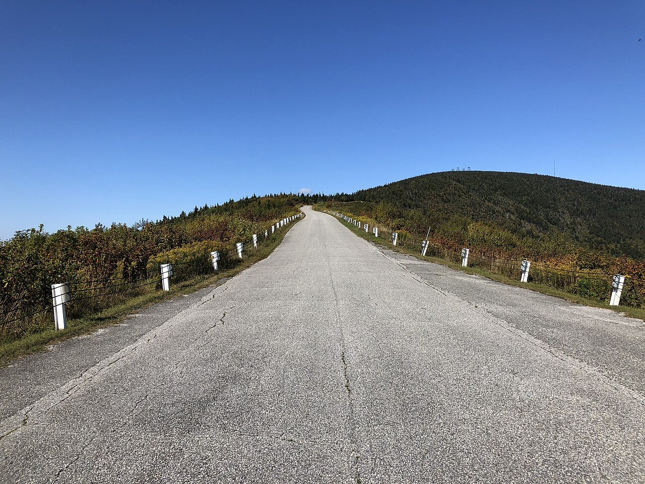 A straight paved road climbing along a ridge toward a wooded summit.