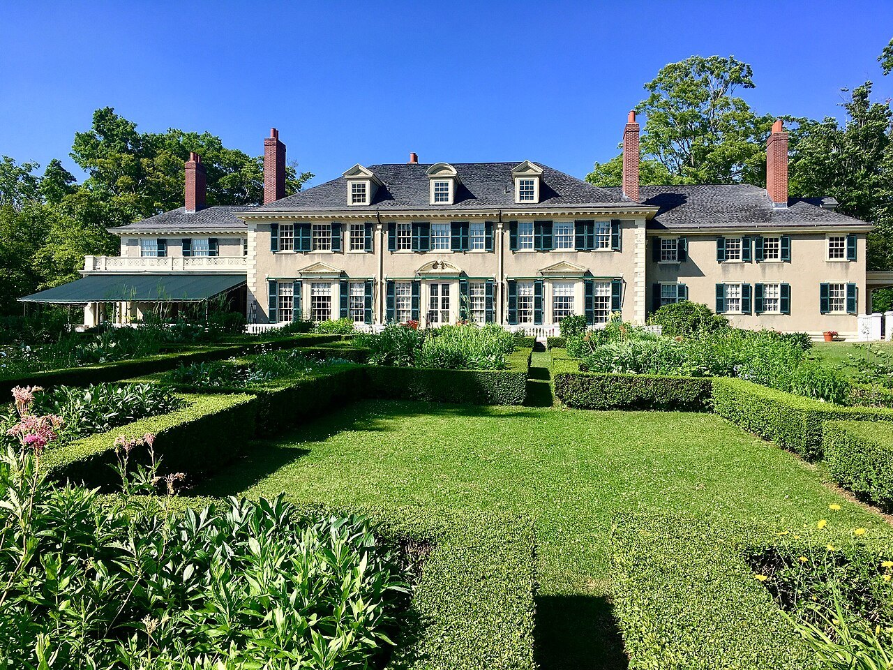 Hildene on a summer day, the house above its lawn and borders under a blue sky.