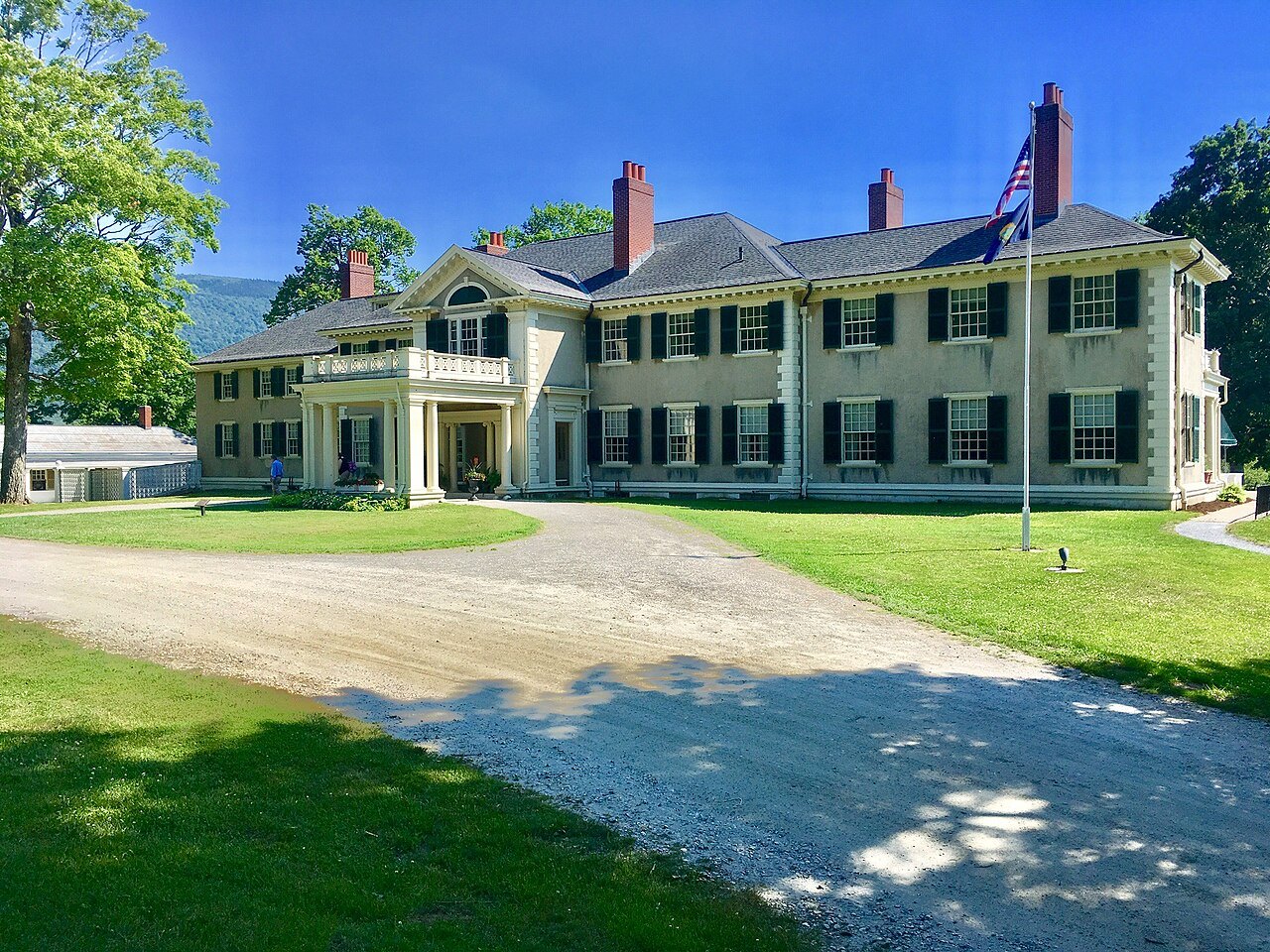The house and its gravel drive in summer, with a flag at the porch.