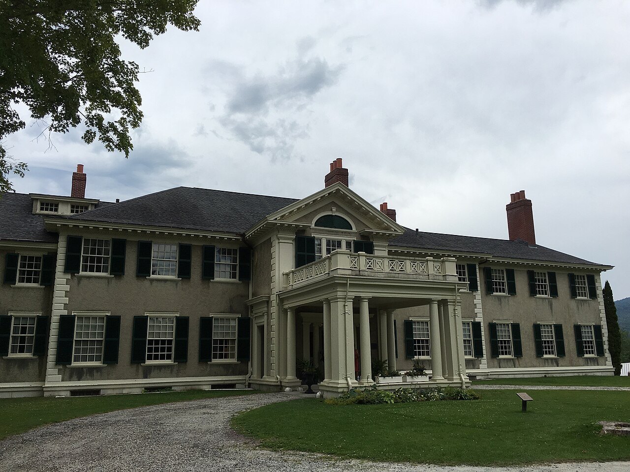 The entrance front of the house, with a columned porch and a gravel drive.