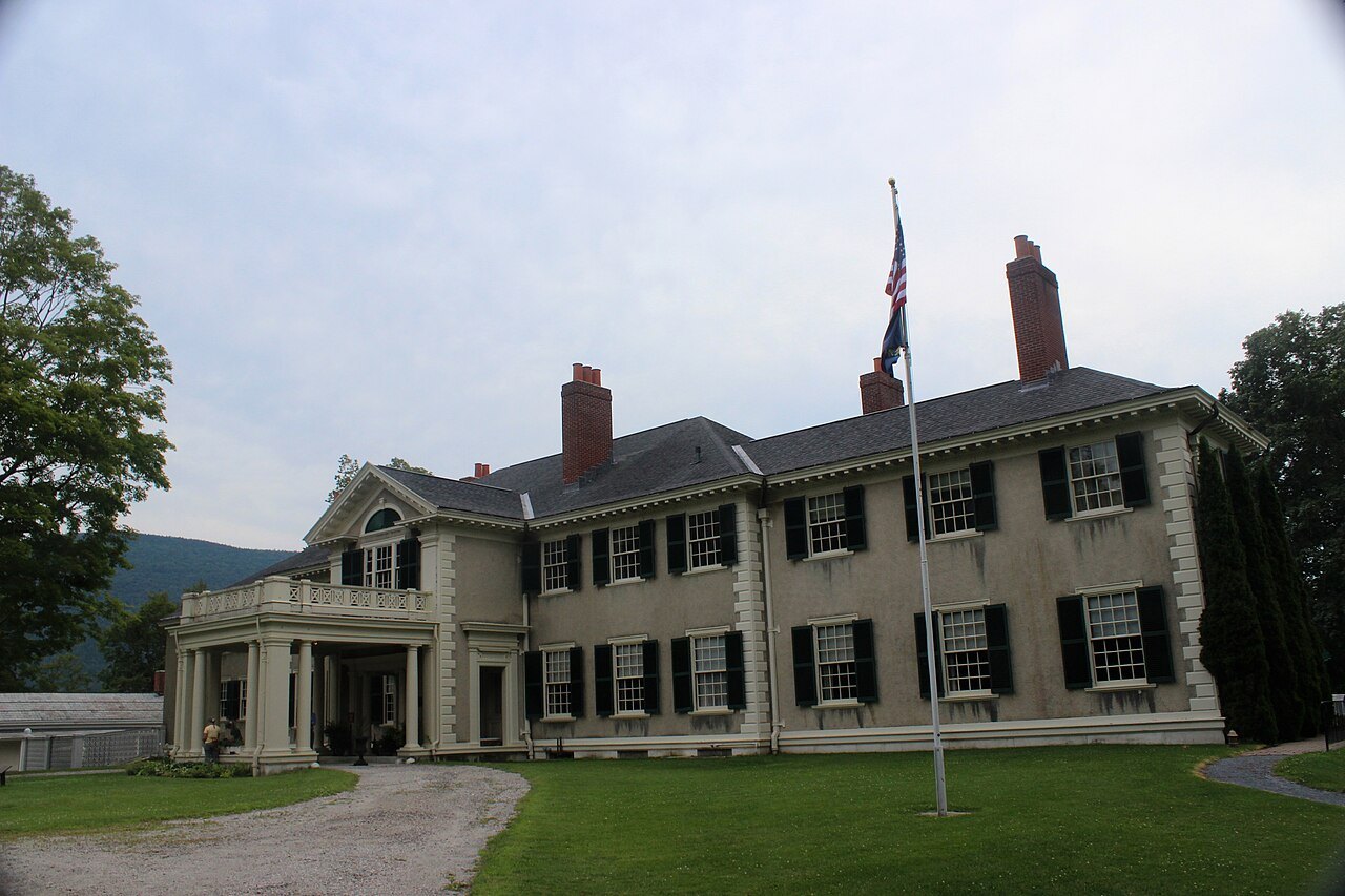 The house from the lawn, a long mansion with dark shutters and a flag.