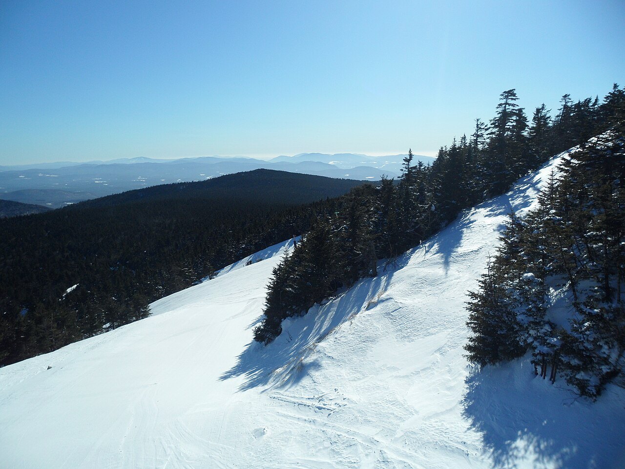 A ski slope at Killington with spruce at its edge and hills beyond.