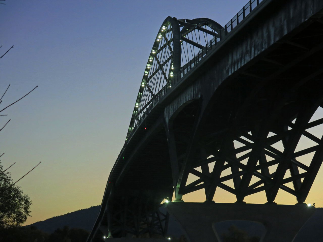 The steel arch of the Lake Champlain Bridge at Chimney Point, against an evening sky.