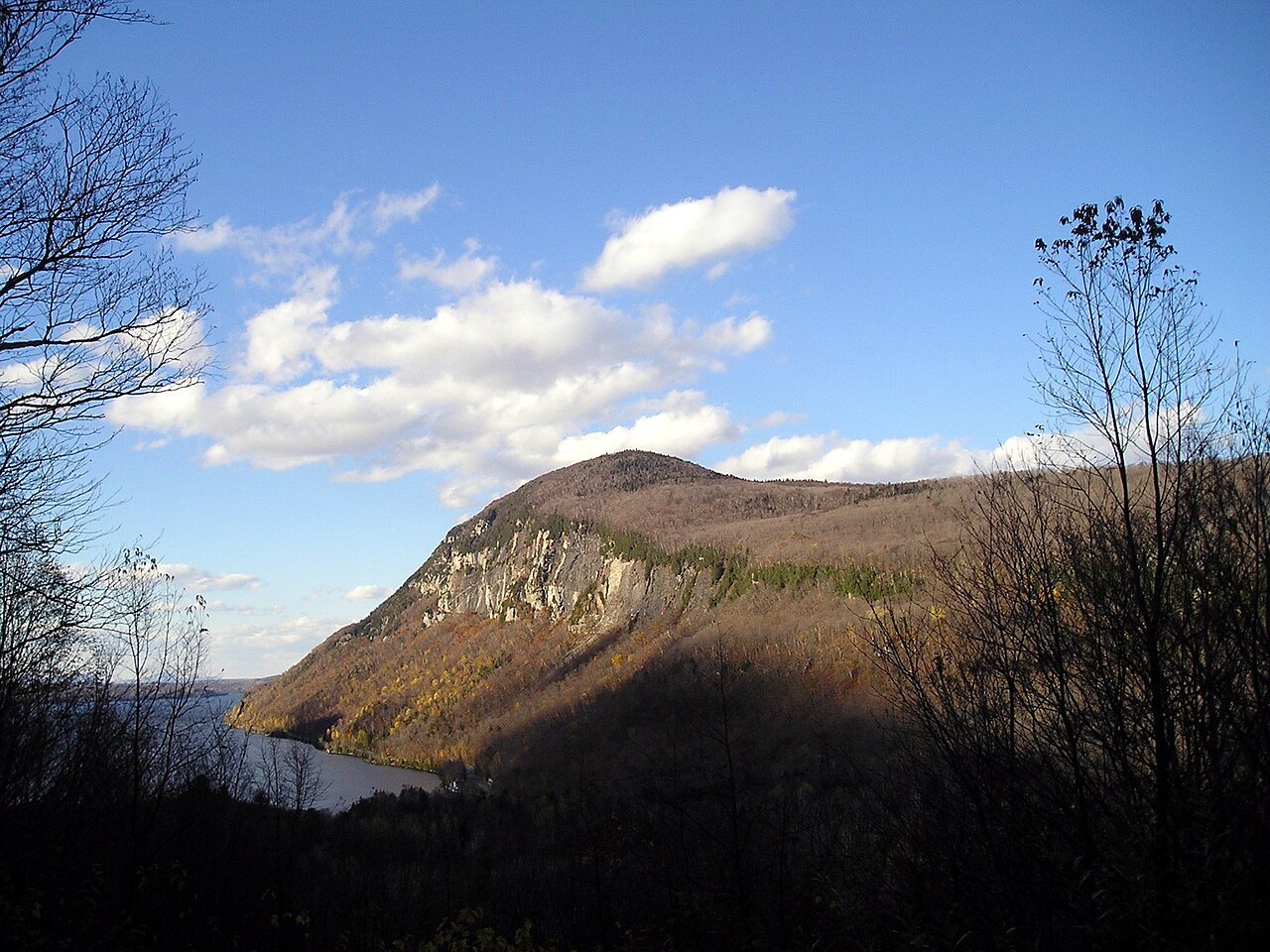 A cliff-faced mountain above Lake Willoughby, seen from the shore road in clear light.