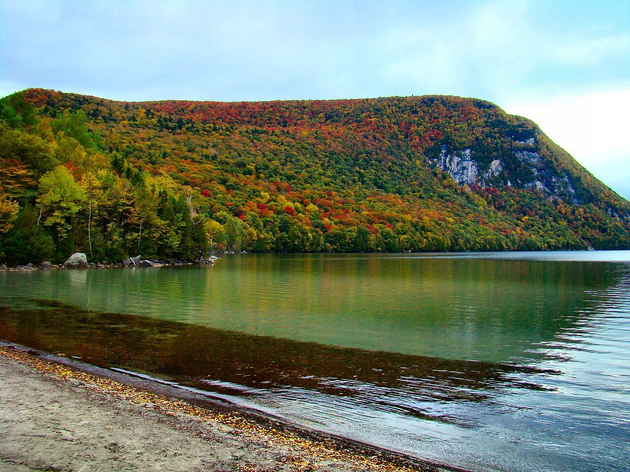 Mount Hor above the lake, forest in autumn color and green water along a pebble beach.