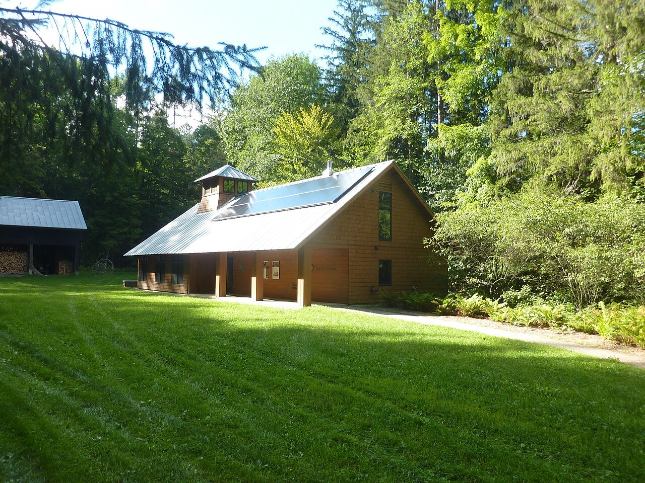 A barn with a solar roof on a mown lawn, under trees.
