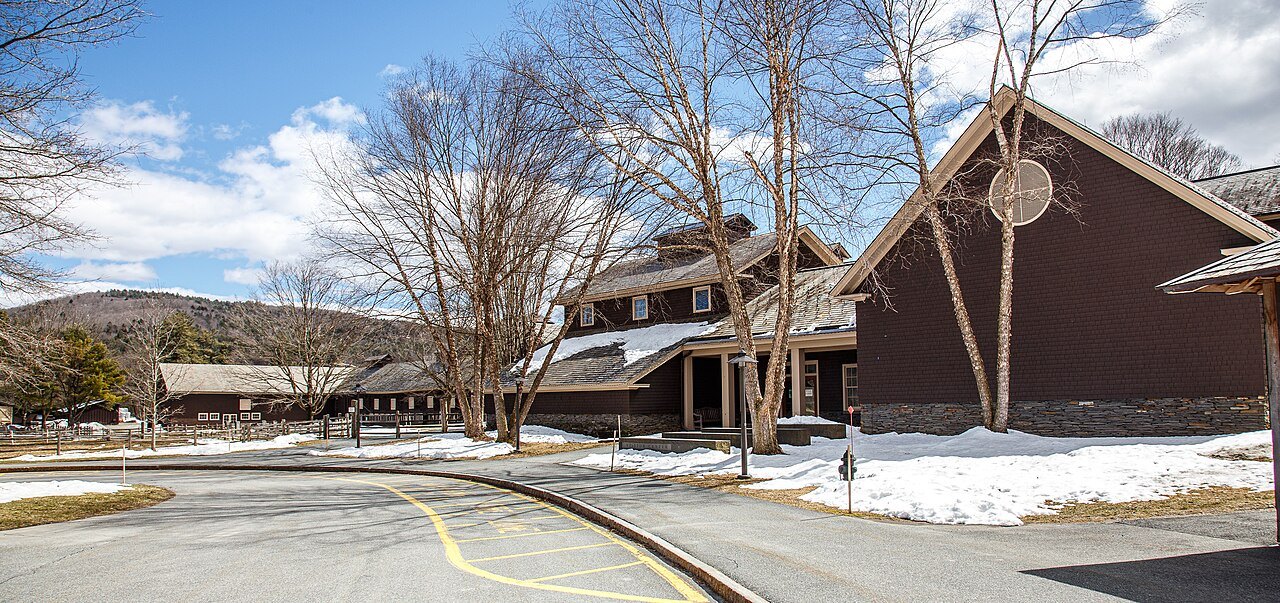 Farm buildings with long brown roofs above a road, with patches of snow on the road.