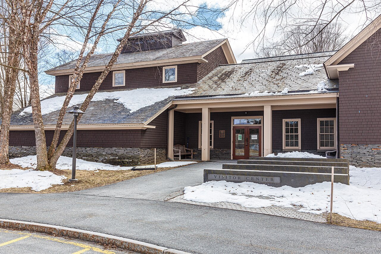 A low wooden complex with deep roofs, seen across a snowy parking area at the farm.