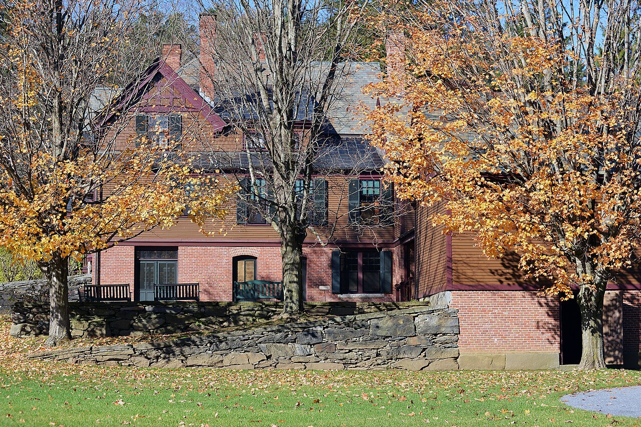 A gabled brick house behind a stone wall in the park at Woodstock, with maples in autumn color.