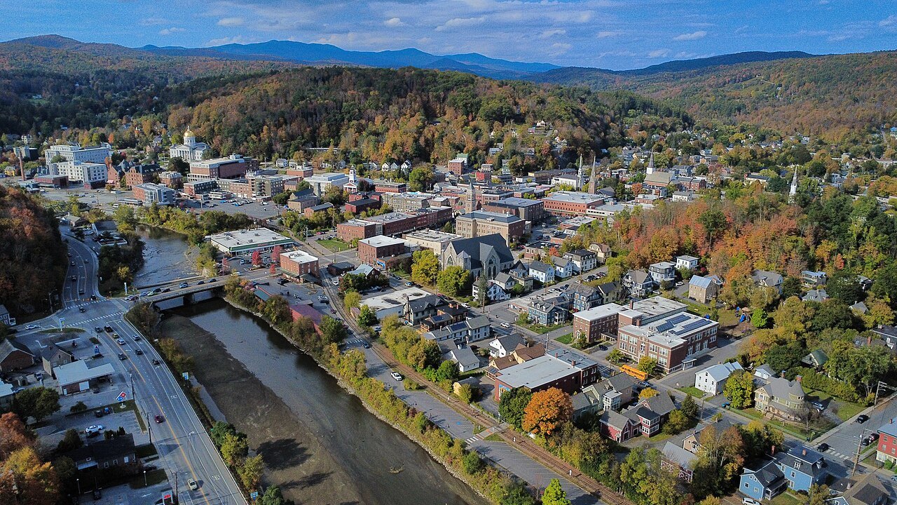 Montpelier from above in autumn, the river running beside a street of brick buildings with hills behind.