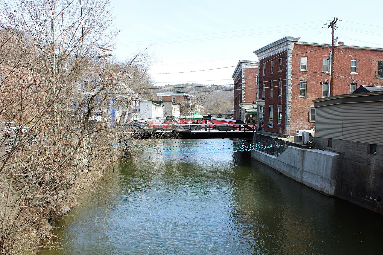 The North Branch of the Winooski River running through Montpelier, with a red footbridge and brick buildings.