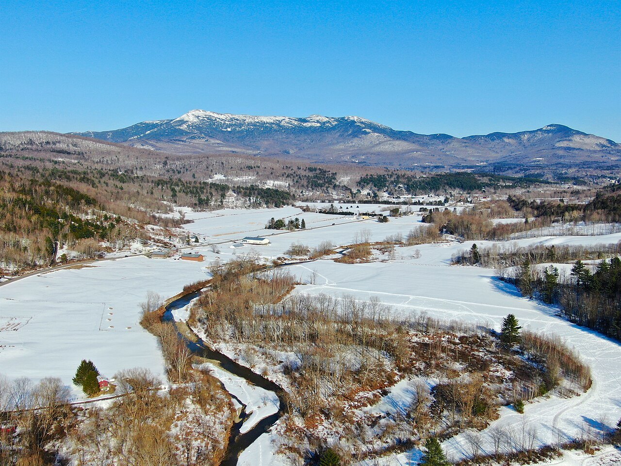 The Mount Mansfield ridge in April, snow on the fields and a stream winding below.