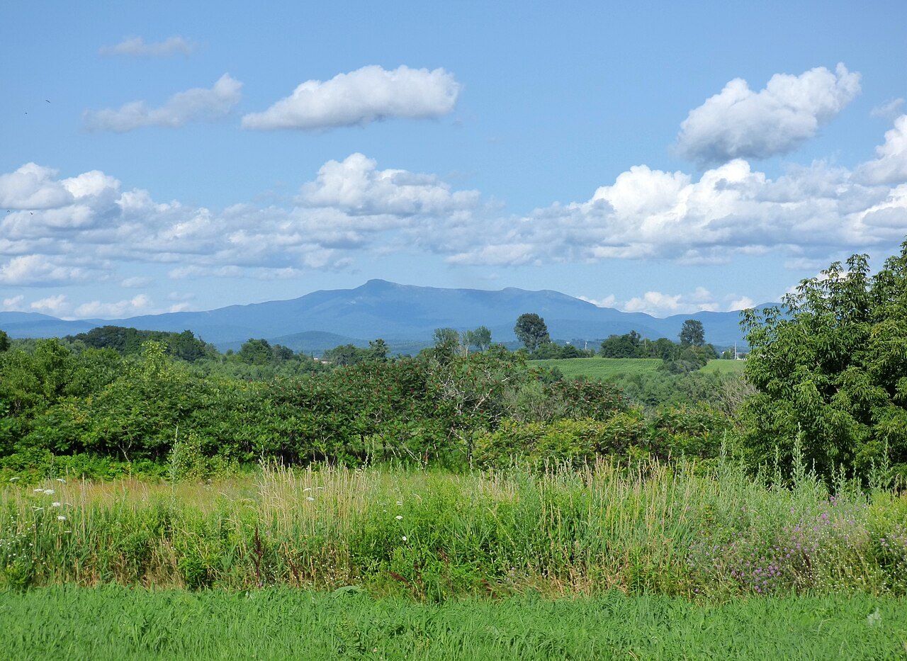 Mount Mansfield from the east above green fields, with the ridge pale and distant.