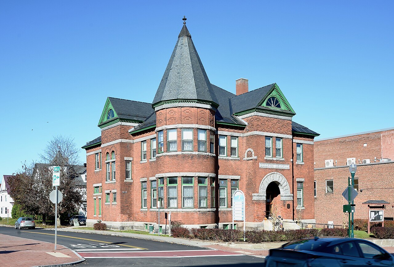 The Goodrich Memorial Library, a red-brick building with a tall pointed tower, on a Newport corner.