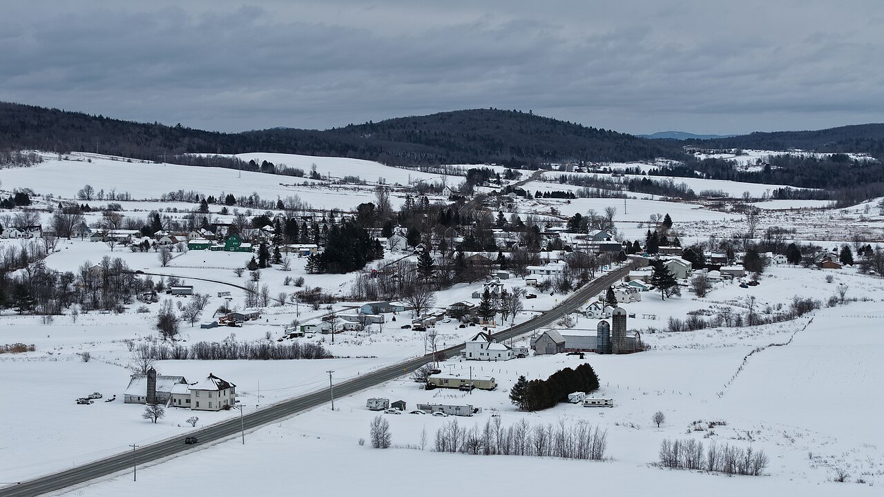 Newport Center in winter from above, snowy farm fields and a road under pale hills.
