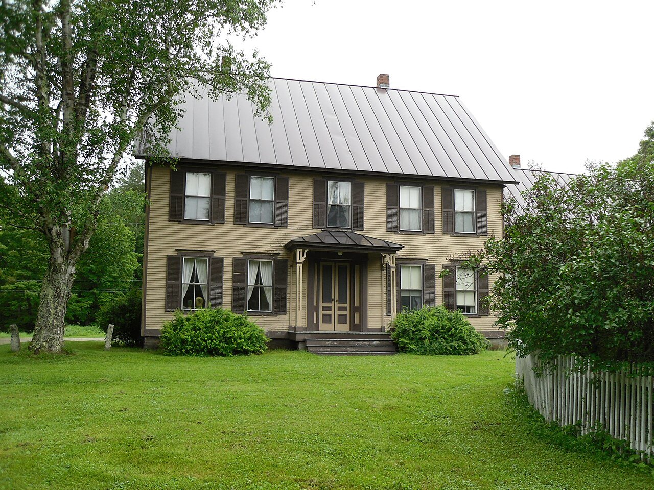 A clapboard farmhouse with a gray metal roof on a lawn at the state historic site.