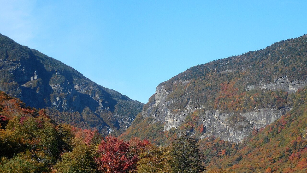 Smugglers' Notch in October, cliffs rising above red and orange slopes.