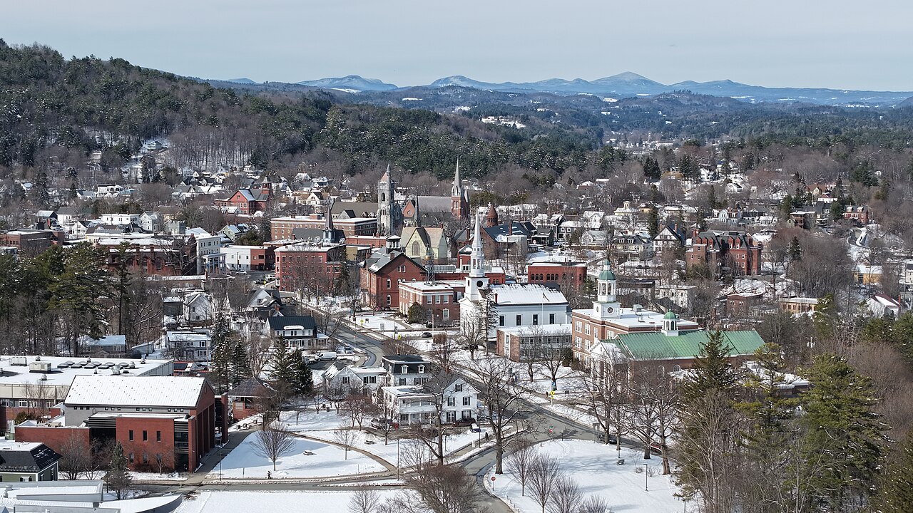St. Johnsbury in March from above, snow on the roofs and spires among the trees.