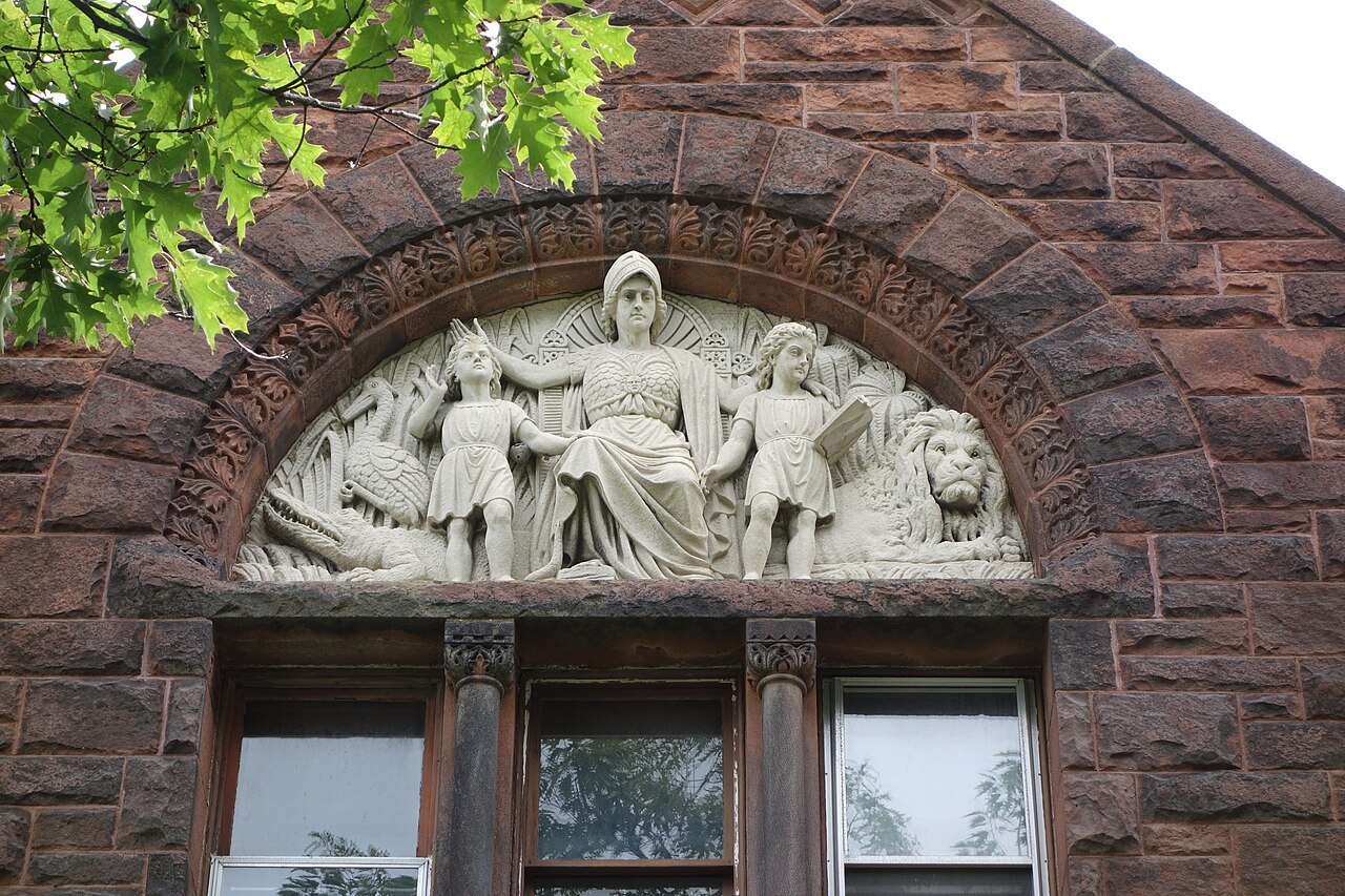 A relief carved in the stone above the museum door, figures seated beneath an arch.