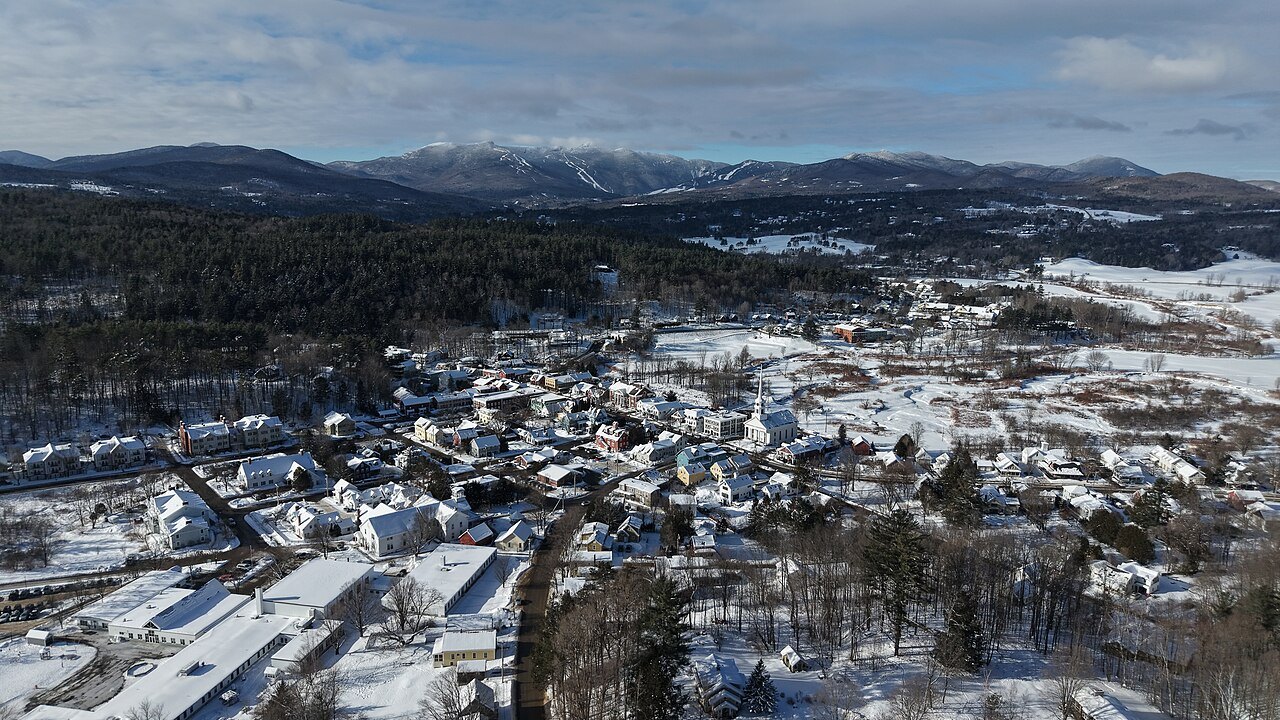 Stowe in winter from above, snow-covered fields and rooftops under the white ridge of Mount Mansfield.