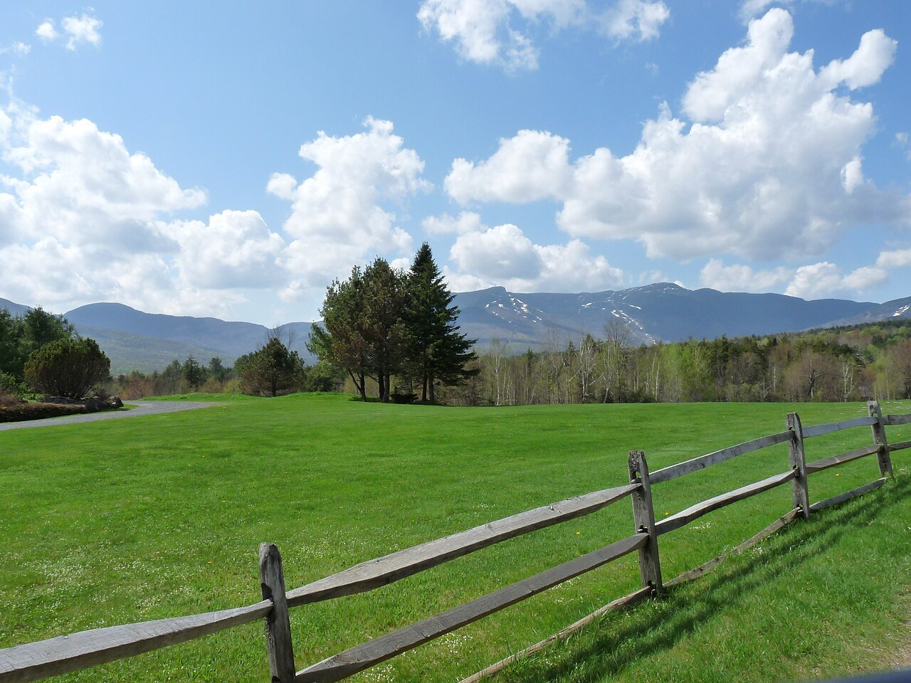 A green field behind a split-rail fence, with the Mansfield ridge in the distance under cloud.